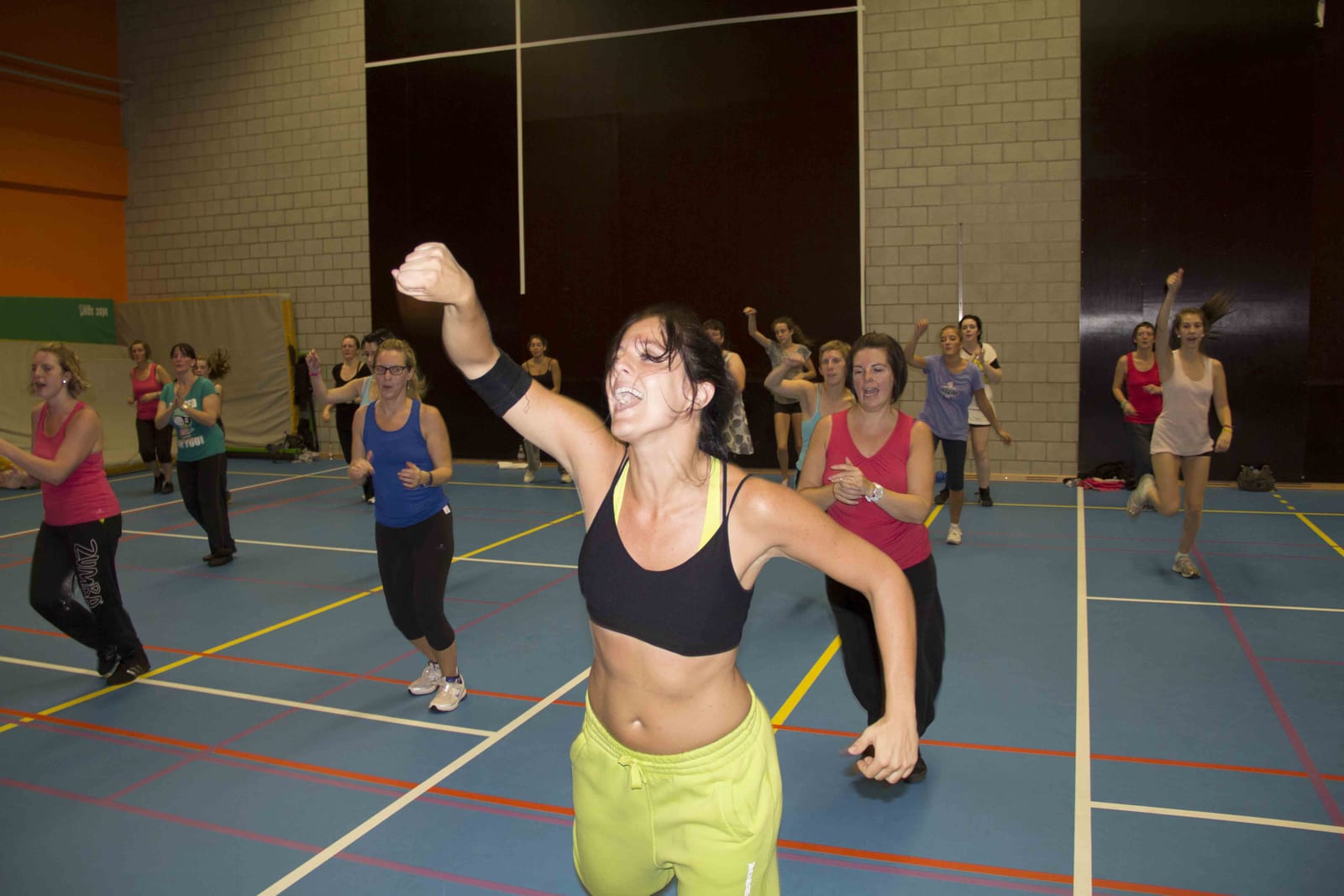 Une coach de DC Fitness mène le cours poing levé, le groupe derrière elle, au Hall Omnisport de Ciney